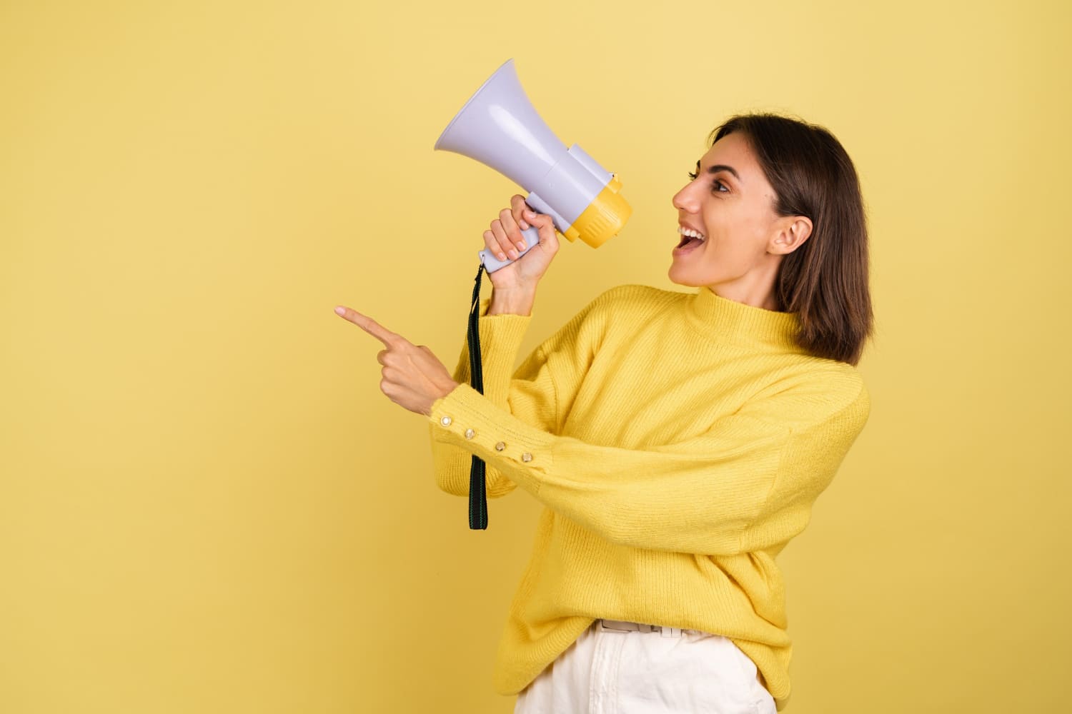 young woman in yellow warm sweater with megaphone speaker screaming to the left pointing index finger 1